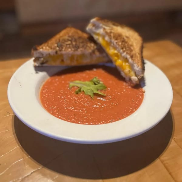 Grilled cheese sandwiches with melted cheese and a bowl of tomato soup with a green garnish.