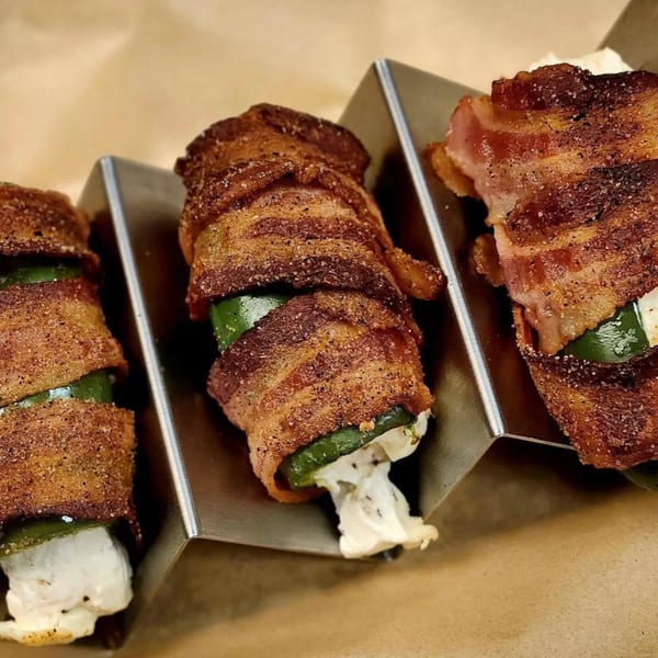 Three bacon-wrapped jalapeño poppers with melted cheese in a metal serving tray.